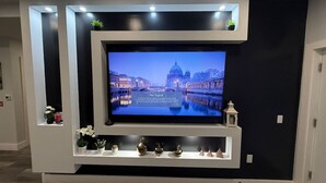 A modern entertainment unit with a flat-screen TV, decorative items, and built-in lighting. - The Luxury Suite: 1BR Perfect for Long Stays (Paterson)
