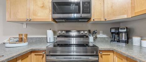 A kitchen with wooden cabinets, a stainless steel microwave, oven, and coffee maker.