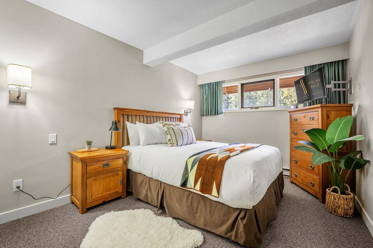 A bedroom with a bed, nightstand, dresser, and a window with curtains.