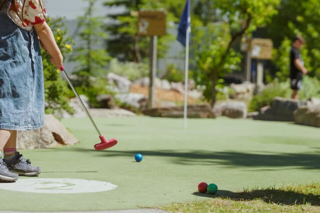 A person playing golf on a course with a putting green, a flag, and a flagpole in the background.