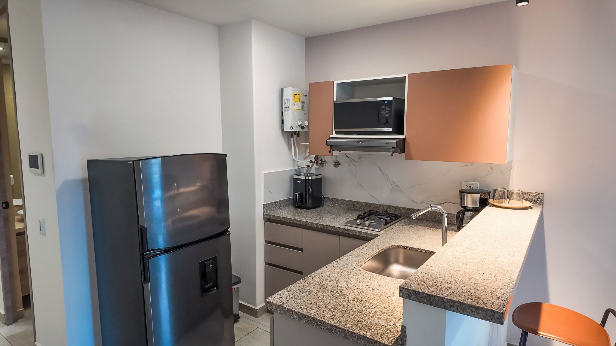 Una cocina moderna con microondas integrado, refrigerador de acero inoxidable y encimera de granito.