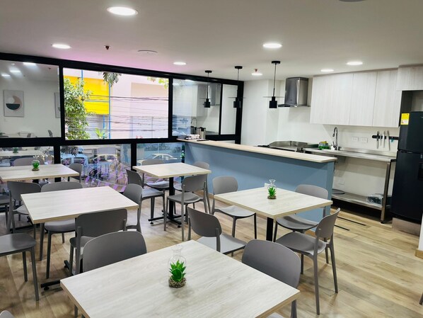 A modern restaurant with tables and chairs, a kitchen area, and large windows. - Hotel Molinos by Growing Group (Medellín)