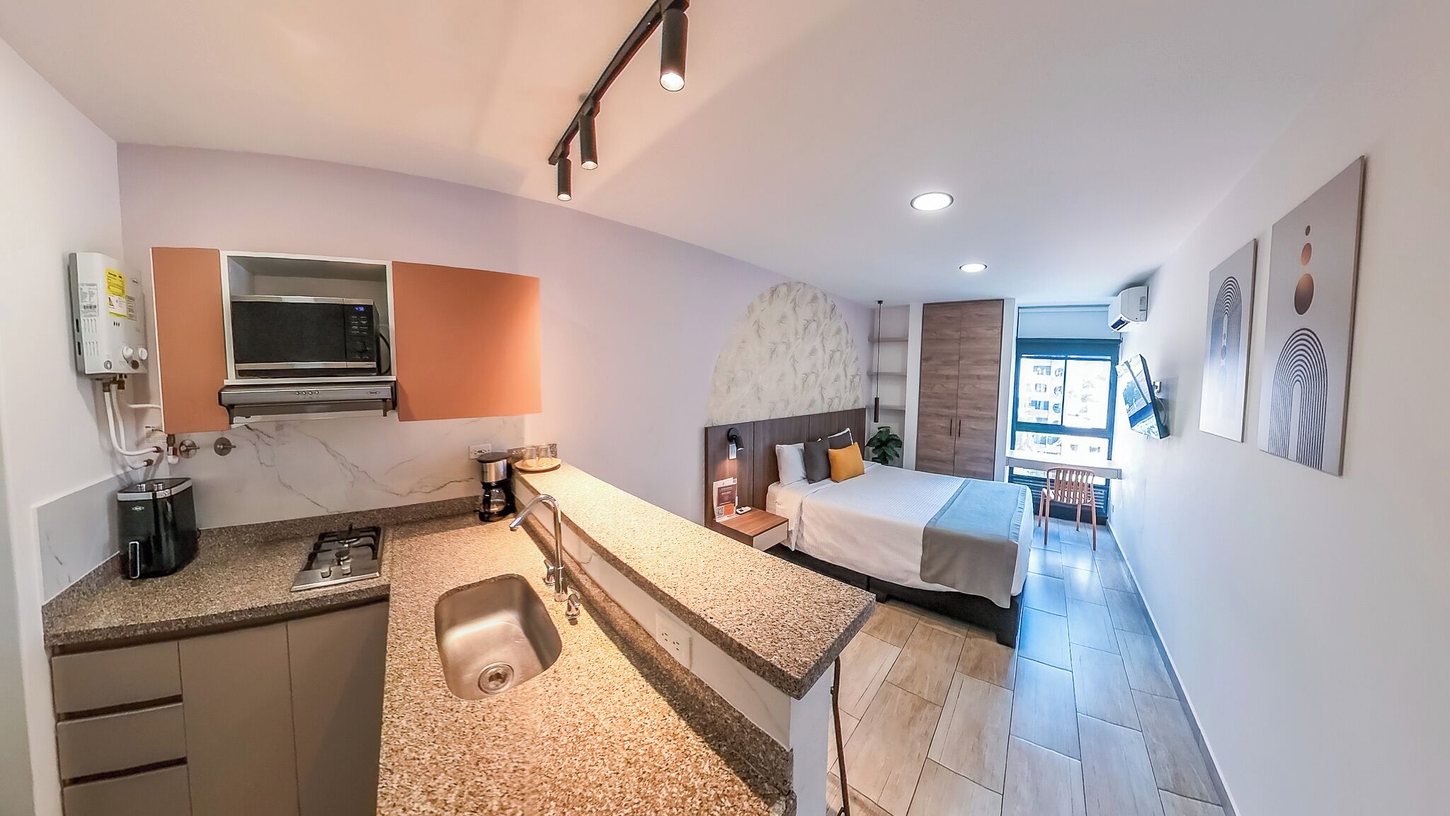 A compact hotel room with a kitchenette, a bed, and a small sitting area.