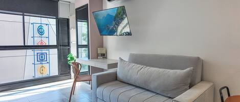 A modern living room with a grey sofa, a flat-screen TV mounted on the wall, a small table, and a chair.