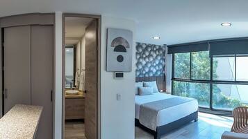 Ein modernes Schlafzimmer mit einem großen Bett, Blick auf Grün hinter einem Fenster und einem Badezimmer mit Dusche und Waschbecken.