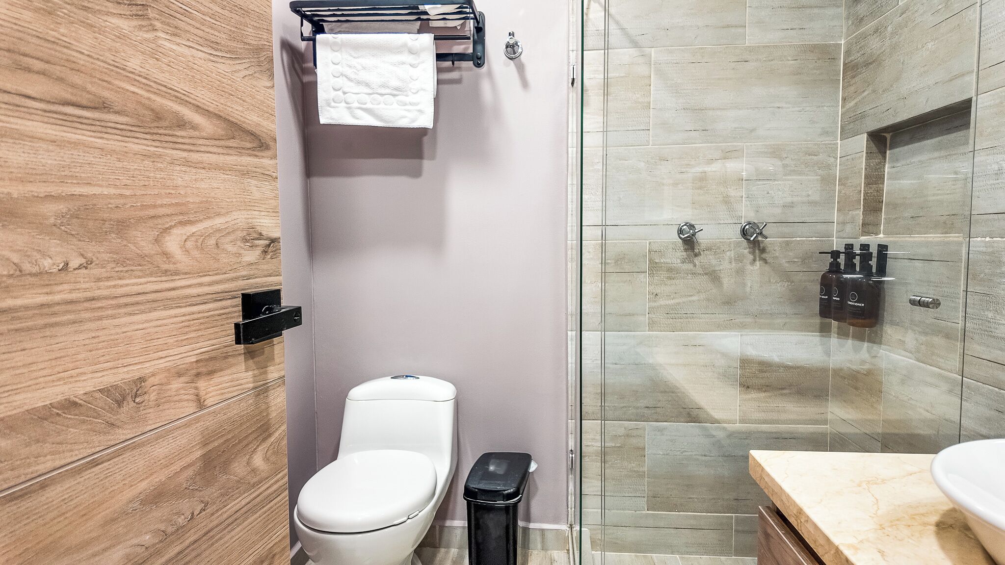 Un baño moderno con inodoro, cabina de ducha de vidrio y tocador de madera.