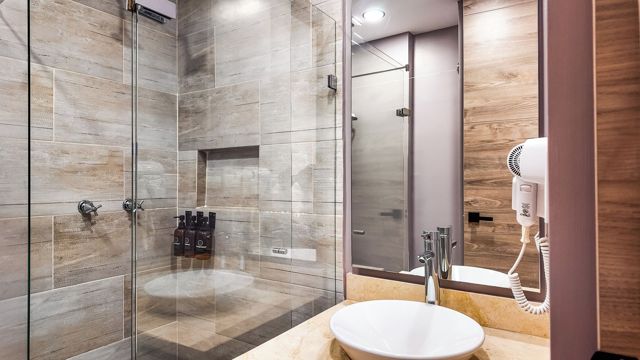 A modern bathroom with a glass-enclosed shower, a white sink, and a hairdryer on the counter.