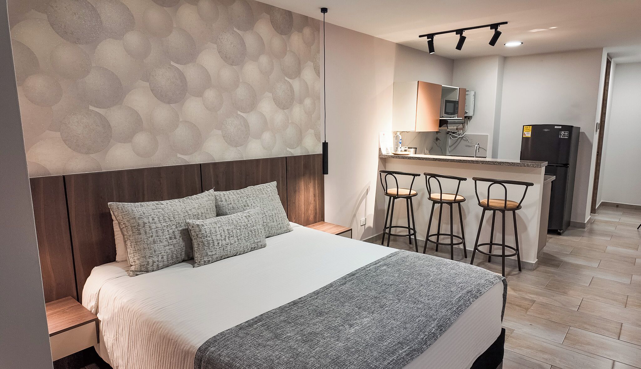 A bedroom with a bed, a headboard, a small bedside table, and a wall with a circular pattern.