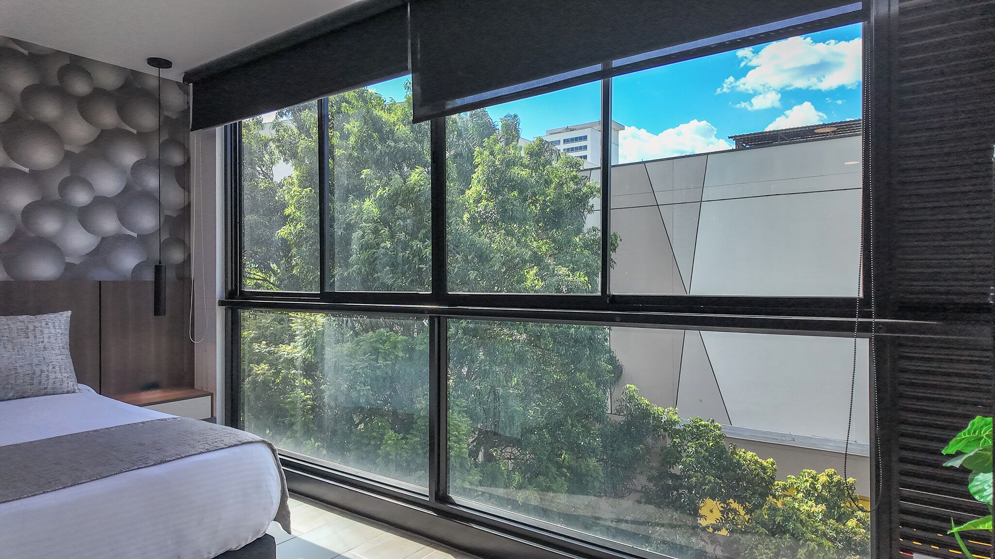 A bedroom with a large window, a bed, and a wall with a geometric pattern.
