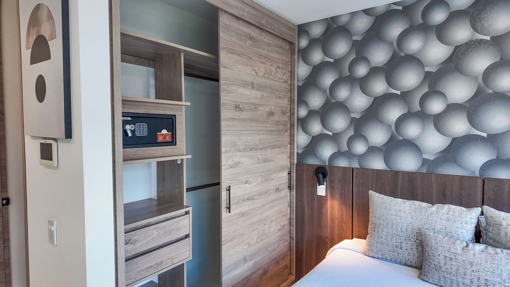 A bedroom with a bed, a nightstand, a wall-mounted light, and a built-in safe.