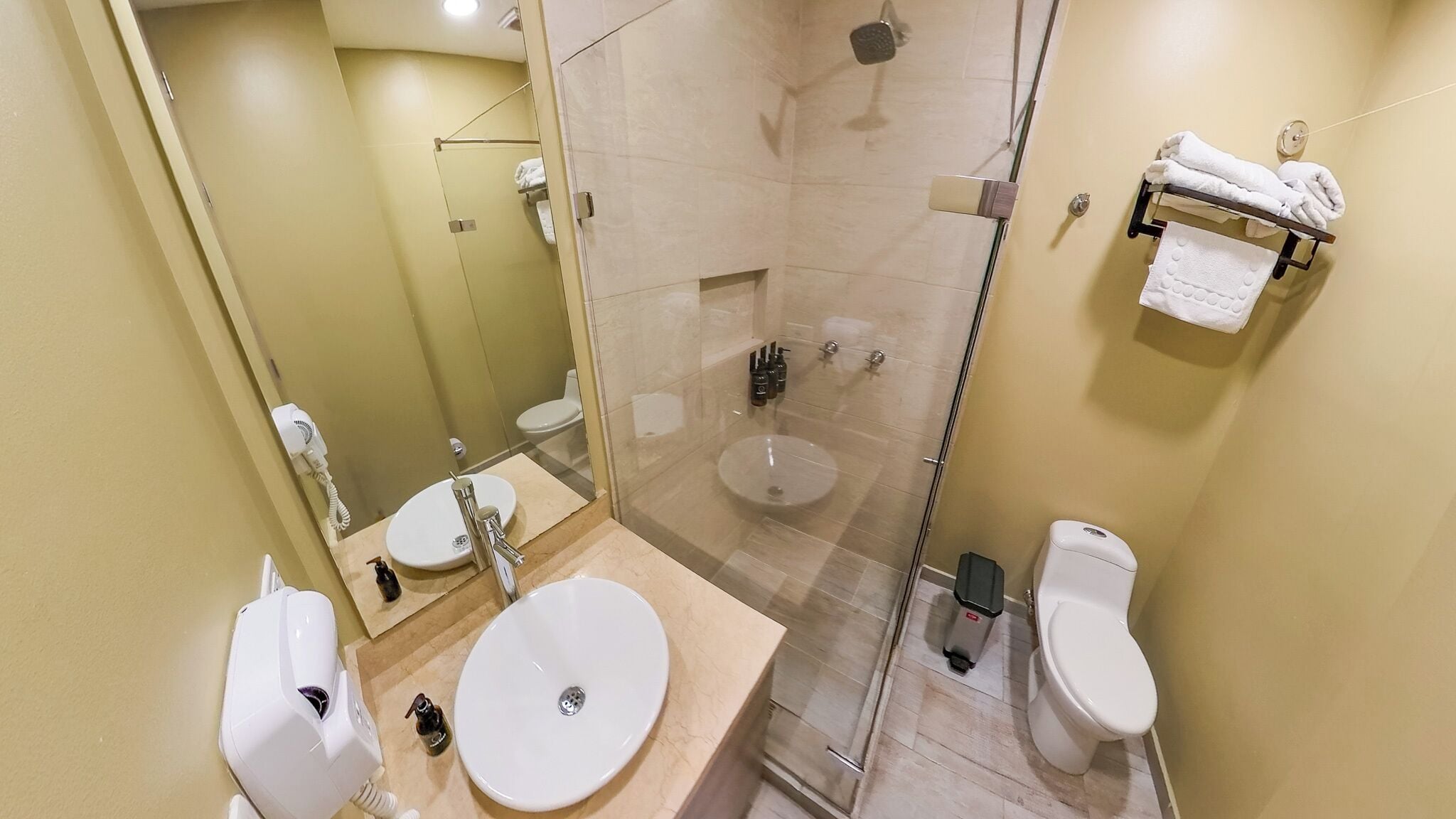 Un baño moderno con ducha de vidrio, dos lavamanos y un inodoro.