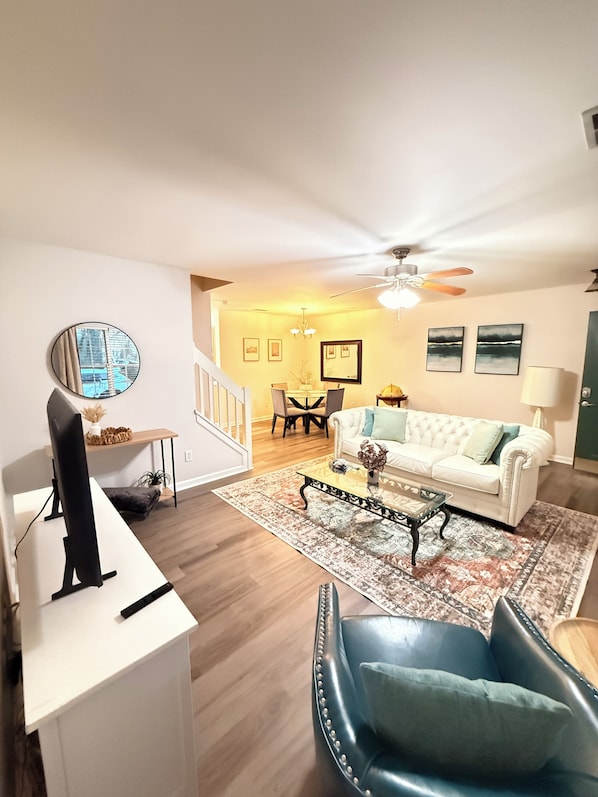 A living room with a white sofa, a blue armchair, a coffee table, and a TV on a white stand.