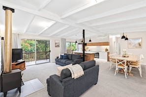 A modern living room with a fireplace, a television, and a sofa. There is a dining area with a table and chairs.