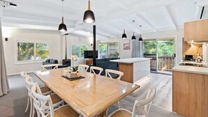 Une cuisine spacieuse avec un îlot central en bois, des chaises blanches, des luminaires suspendus et de grandes fenêtres.