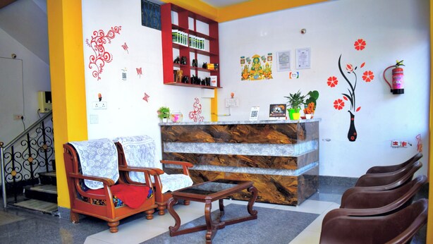 Un espace d’accueil comprenant un comptoir de réception en bois, une bibliothèque rouge et un coin salon avec des fauteuils marron.