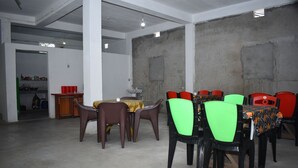 Une pièce spacieuse avec un plafond haut, un coin repas avec des chaises en plastique et une table, et une cuisine visible à travers une porte ouverte.