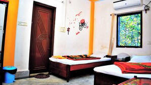 Une chambre avec deux lits, une fenêtre ornée d’une grille décorative, un appareil de climatisation et un mur décoré d’un motif floral.