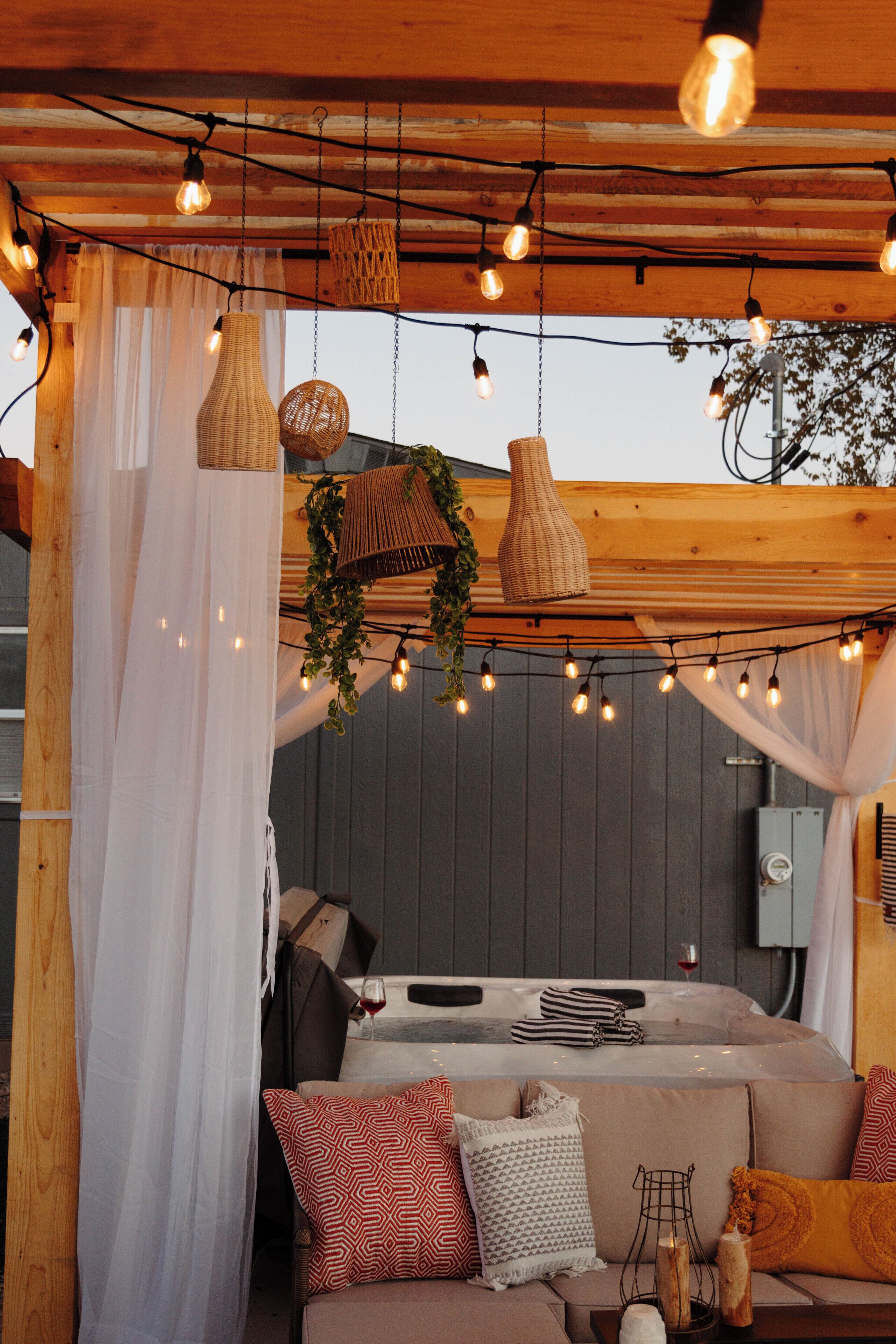 Una zona de estar al aire libre acogedora, con un porche de madera, luces cálidas y un sofá con cojines estampados.