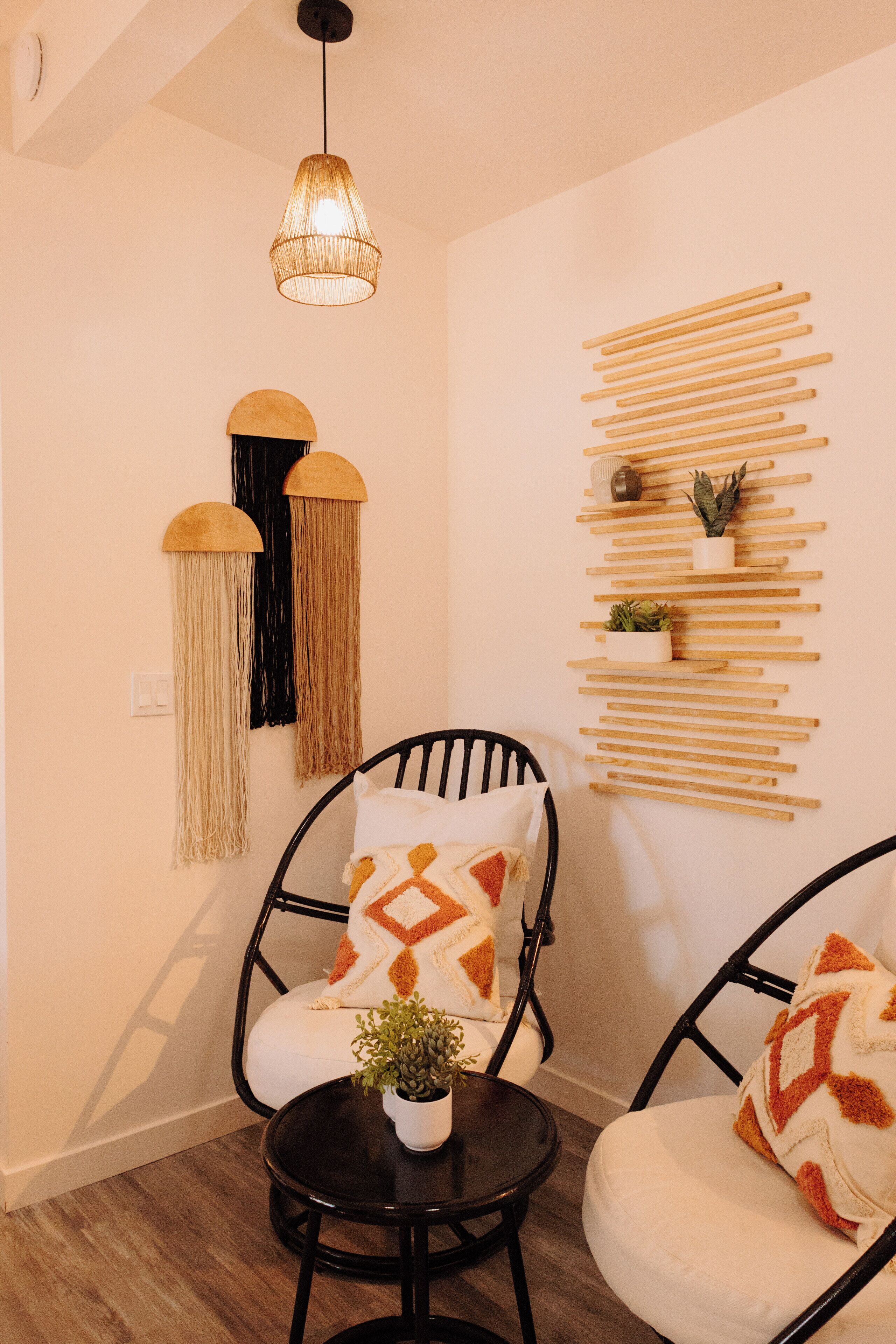 Un coin salon accueillant avec deux chaises noires, une petite table ronde ornée d’une plante, et une étagère en bois fixée au mur, également décorée de plantes.