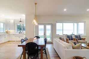 Una cocina moderna con armarios blancos, una mesa de comedor de madera y vistas al exterior a través de amplios ventanales.