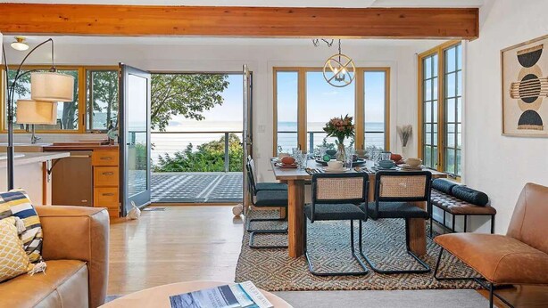 Una habitación amplia con techo de madera, un comedor con mesa y sillas, y grandes ventanas que ofrecen vistas al exterior.