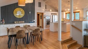A spacious kitchen with a central island, a dining area with a wooden table and chairs, and a staircase leading to an upper level. - Hood Canal Waterfront Group Retreat (Silverdale)
