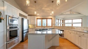 A spacious kitchen with white cabinetry, a large island, stainless steel appliances, and pendant lighting. - Hood Canal Waterfront Group Retreat (Silverdale)