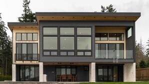 Een modern huis met twee verdiepingen, grote ramen, een balkon en een stenen fundering.