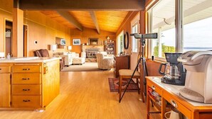 A cozy cabin interior with a wooden floor, a fireplace, a dining area, and a large window offering a view. - An Exciting Salish Escape w/ Waterfront View (Kingston)