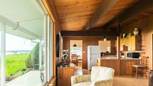 A compact cabin with a kitchen, dining area, and a large window overlooking a grassy area. - An Exciting Salish Escape w/ Waterfront View (Kingston)