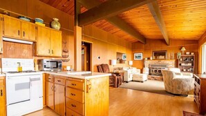 A spacious kitchen with wooden cabinets, a central island, and a dining area with a fireplace. - An Exciting Salish Escape w/ Waterfront View (Kingston)