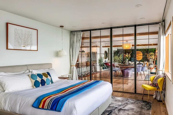 Une chambre moderne avec un grand lit, une vue sur l’espace repas extérieur grâce à des portes vitrées, et une décoration minimaliste.