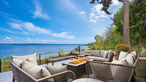 Een terras met rieten meubilair, een vuurkorf en uitzicht op het water.