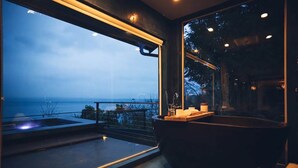 Een moderne badkamer met een groot raam met uitzicht op een balkon en de zee.