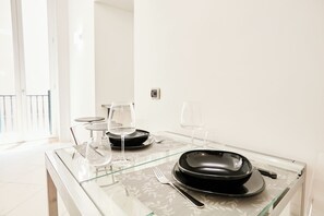 A dining table with a glass top, black plates, and wine glasses.