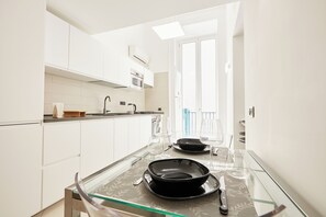 Uma cozinha moderna com armários brancos, uma mesa de vidro e vista para uma varanda.