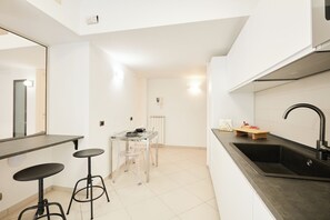 Uma cozinha compacta com uma pia preta, uma pequena mesa de jantar com banquetas e paredes brancas.