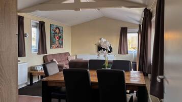 A cozy room with a wooden dining table, black chairs, a brown sofa, and a large window with curtains.