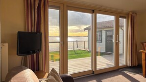 Ein Wohnzimmer mit einer Couch, einem Fernseher und Blick auf eine Terrasse und einen Außenbereich.