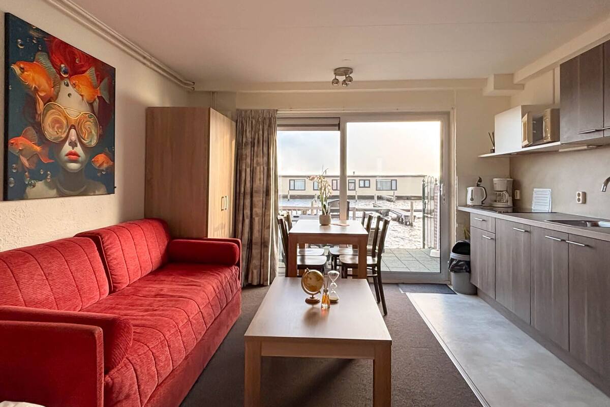 A modern living room with a red sofa, a wooden dining table, and a large window with a view of a building and a balcony.