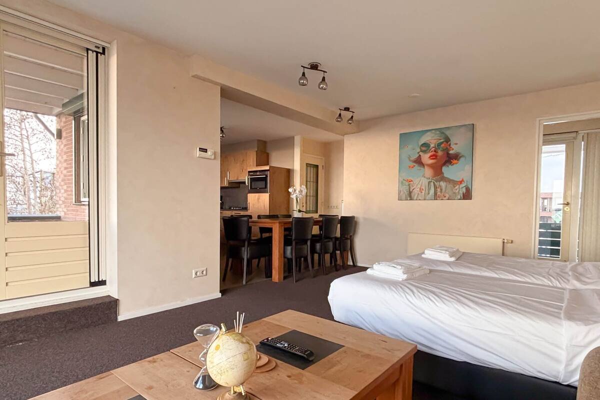A hotel room with a bed, a desk with a globe and remote control, a painting on the wall, and a view of the outside.