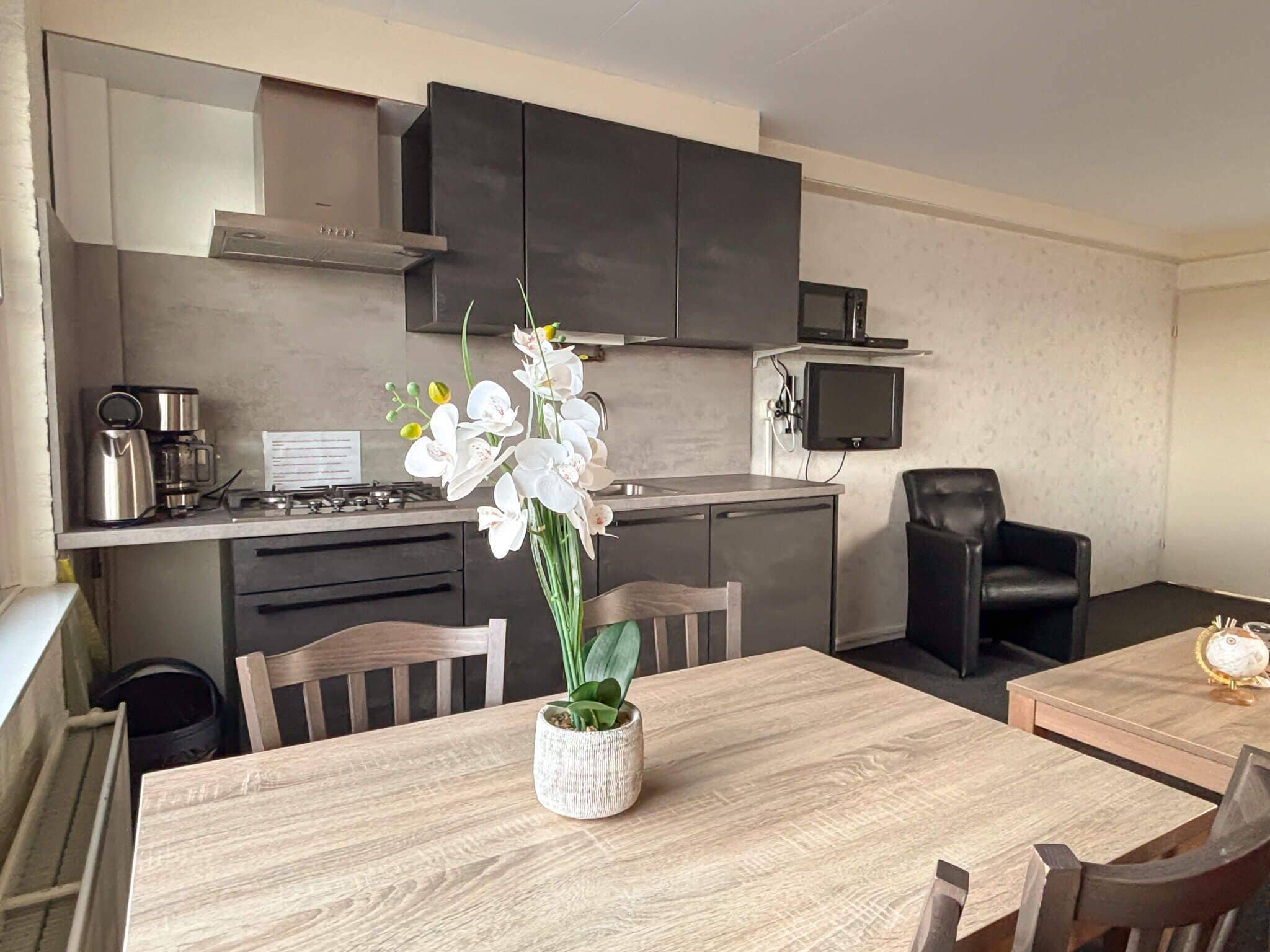 Una cocina moderna con armarios oscuros, una estufa de acero inoxidable y un microondas. Hay una mesa de comedor de madera con sillas y un jarrón con orquídeas blancas.