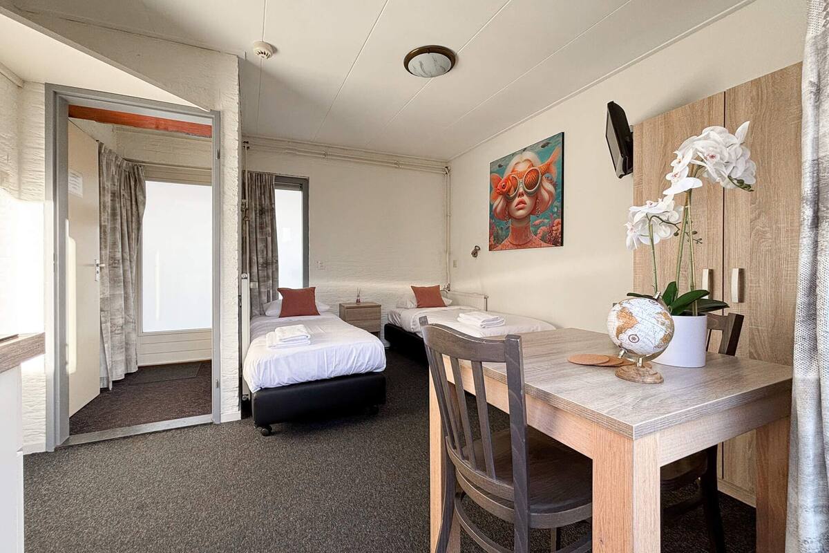 A hotel room with a bed, a desk with a globe, and a painting on the wall.