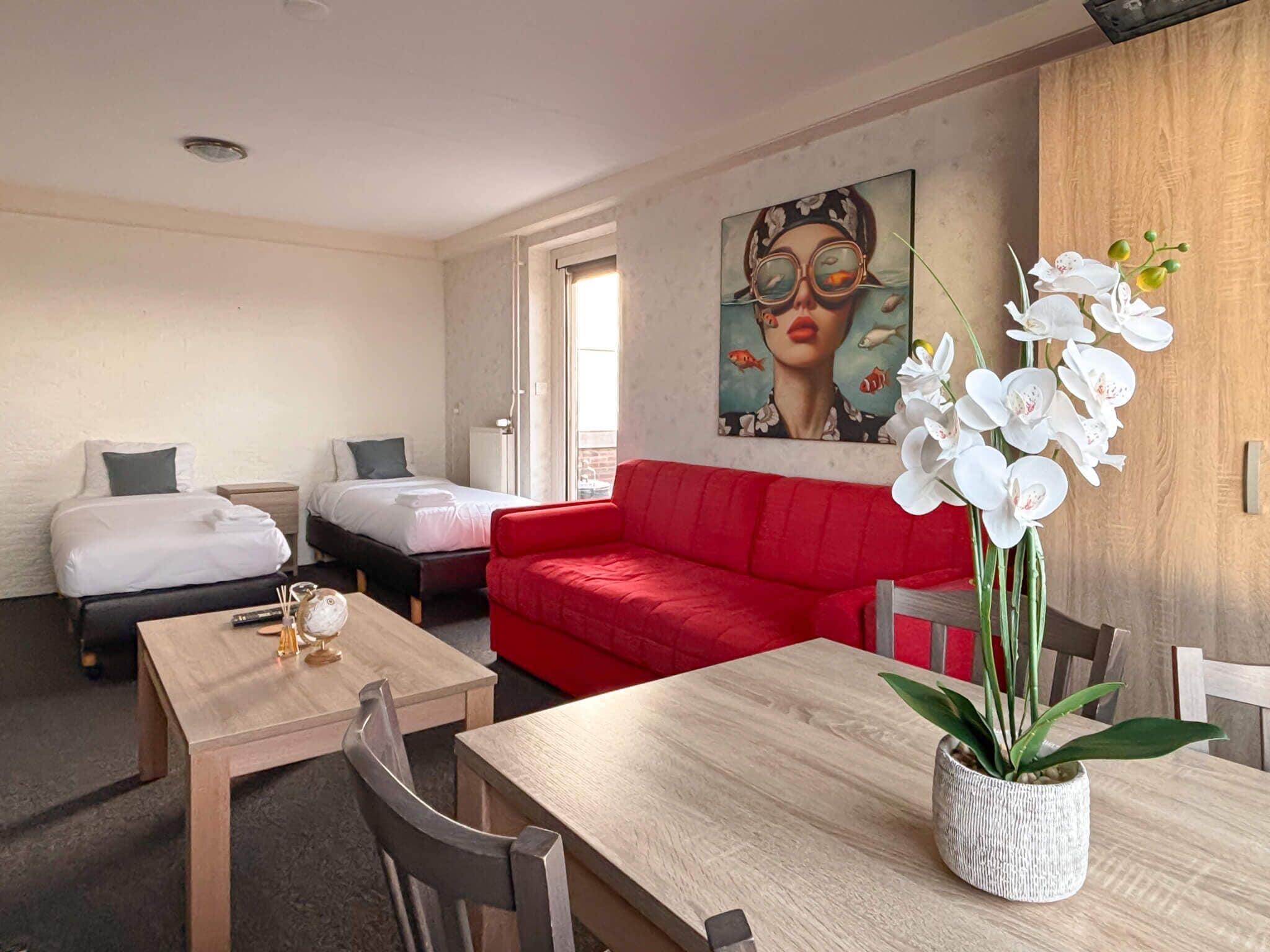 Une chambre d’hôtel avec deux lits, un canapé rouge, une table en bois et un tableau au mur.