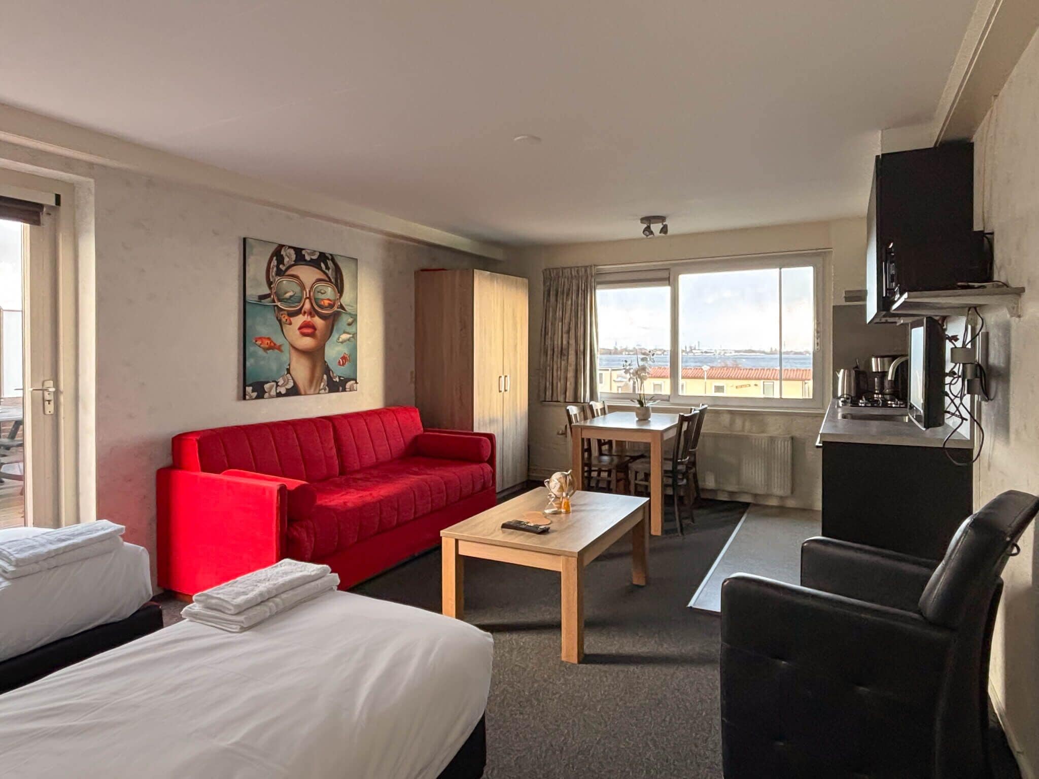 A hotel room with a red sofa, a wooden table, a TV, and a view of the city through the window.