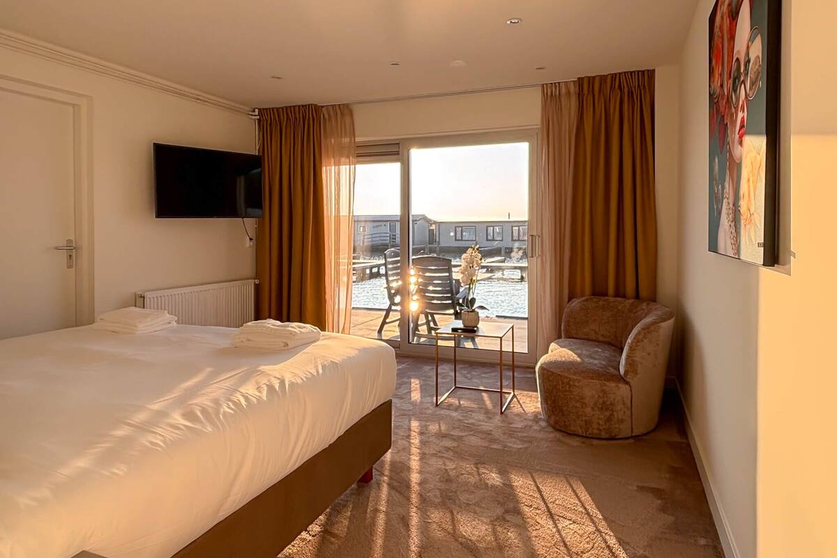 A hotel room with a bed, a chair, a TV, and a view of the outside.