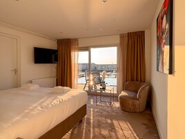 Quarto de hotel com cama, uma cadeira, televisão e vista para o exterior.