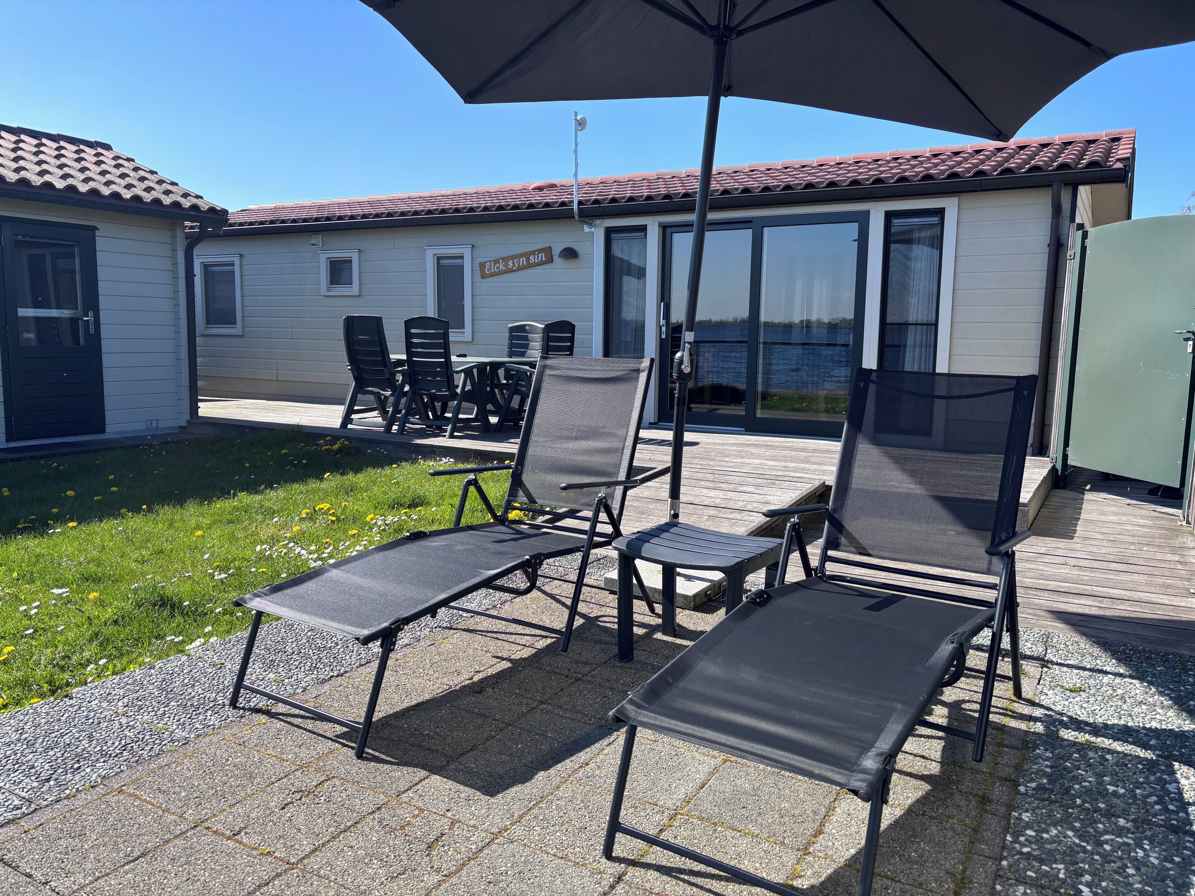 Een terras met buitenmeubilair, waaronder stoelen en een tafel, onder een grote parasol.