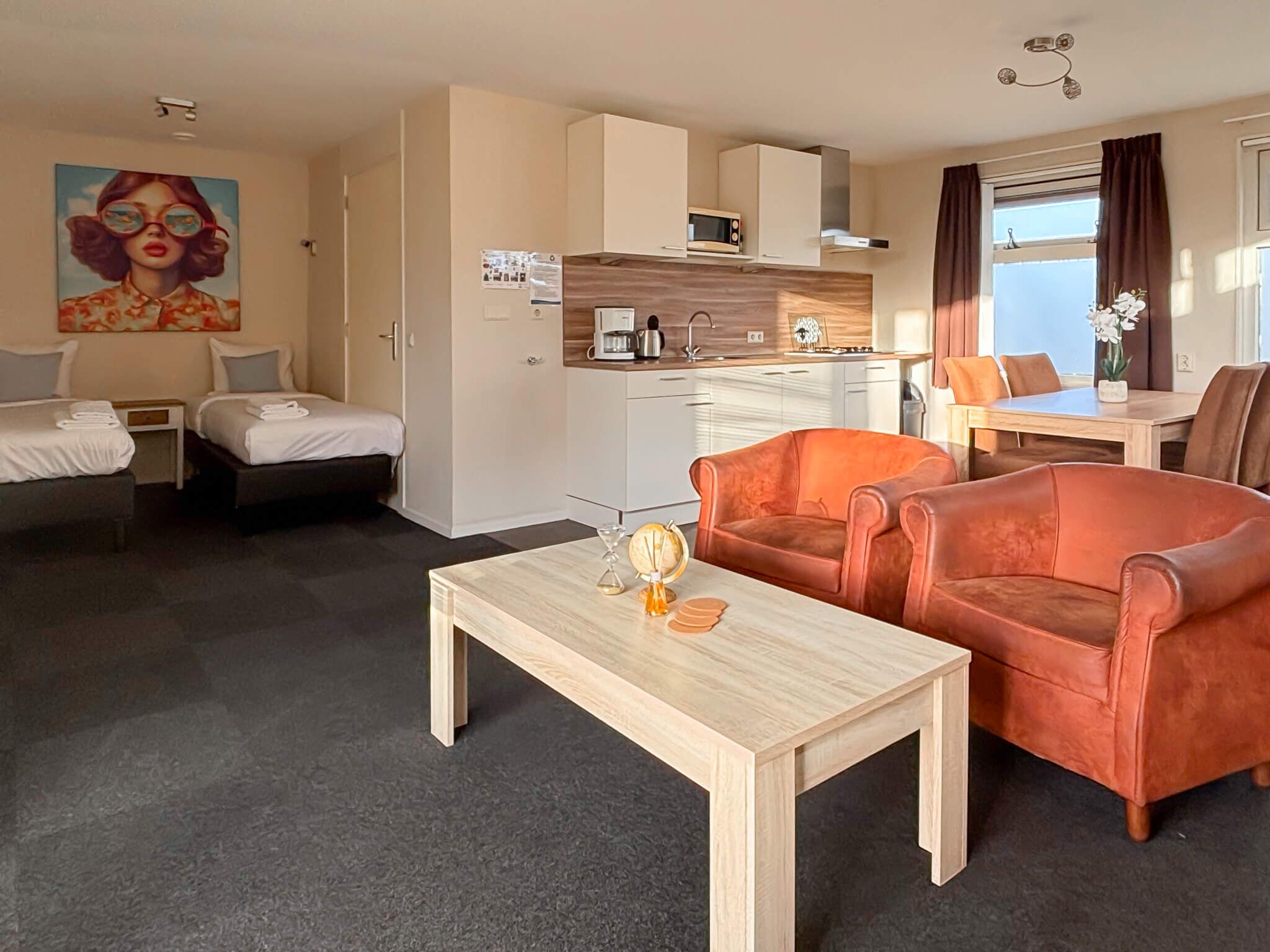 A compact hotel room with a kitchenette, a dining area, and two single beds.