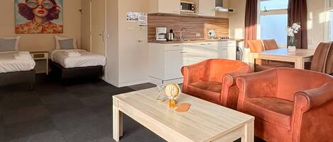 A compact hotel room with a kitchenette, a dining area, and two single beds.